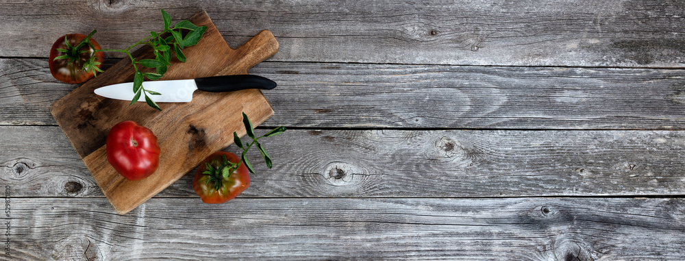 Ripe organic tomatoes with cutting knife plus server on rustic wooded table Ripe organic tomatoes with cutting knife plus server on rustic wooded table