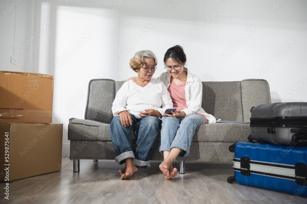 Asian old woman and teenage woman, mother and daughter, sitting on a sofa watching content on a smartphone screen together, the concept of Moving home on a budget.