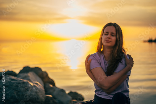 portrait of a woman hugging herself at sunset in summer by the sea photo