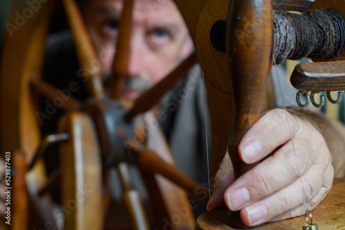 Skilled tradesman works to repair and to intricately fettle the mechanism of an old wooden spinning wheel. Selective focus to accentuate the task of repair and service. Contrasting lighting