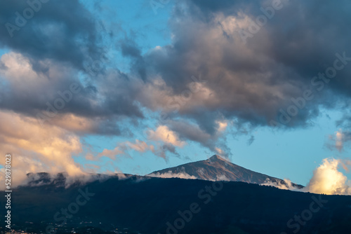 Panoramic view on the peak of volcano Pico del Teide during sunset seen from the port of Puerto de la Cruz, Tenerife, Canary Islands, Spain, Europe. The summit turns vibrant red during golden hour