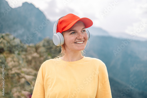 Happy young female traveler with blonde hair in red hat listens to favorite music in wireless headphones smiles. 