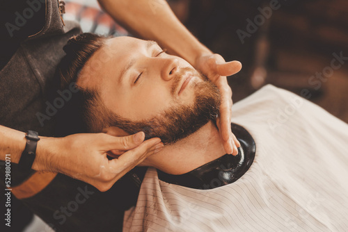 Fototapeta Hairdresser massages man face to improve hair growth and skin care