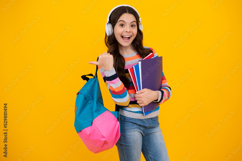 Amazed teenager. Schoolgirl, teenage student girl in headphones hold books on yellow isolated studio background. School and music education concept. Back to school. Excited teen girl. Amazed teenager. Schoolgirl, teenage student girl in headphones hold books on yellow isolated studio background. School and music education concept. Back to school. Excited teen girl.