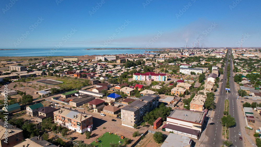 The small town of Balkhash is a view from a drone. A city in the middle of the steppe on the shore of Lake Balkhash. The metallurgical plant is smoking. Bad ecology. Low monotonous houses. Cars drive