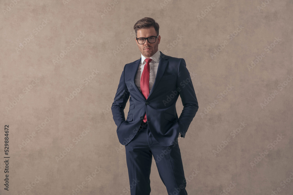 confident young guy in elegant suit with glasses holding hands in pockets confident young guy in elegant suit with glasses holding hands in pockets