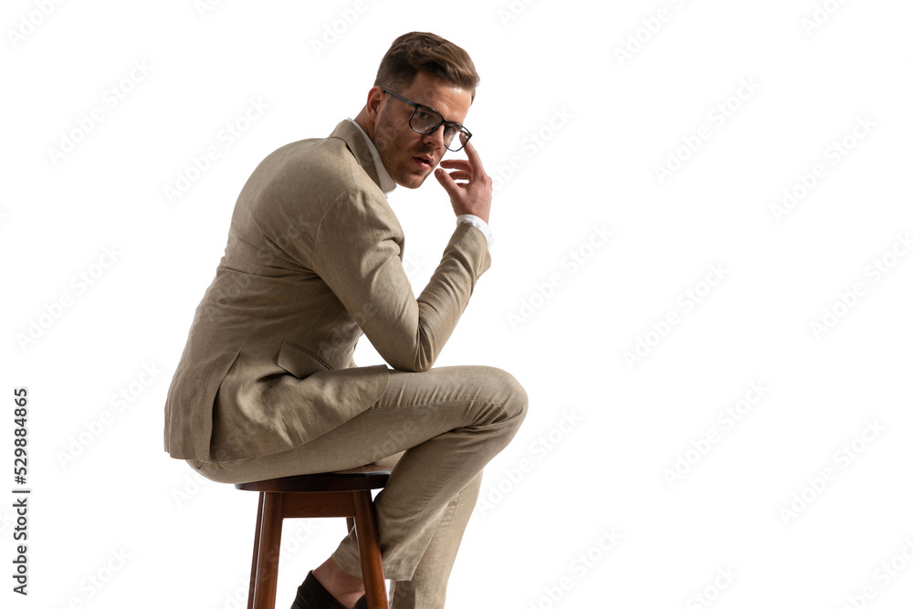 side view of attractive businessman sitting on wooden chair and adjusting glasses side view of attractive businessman sitting on wooden chair and adjusting glasses