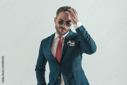 happy unshaved man in suit with retro sunglasses adjusting hair photo