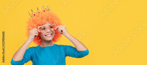 happy funny kid in curly wig and crown. imagine herself a queen. cheerful child wear diadem. Funny teenager child in wig, party poster. Banner header, copy space.