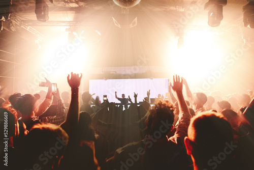 DJ performing at nightclub with crowd of people with their hands up