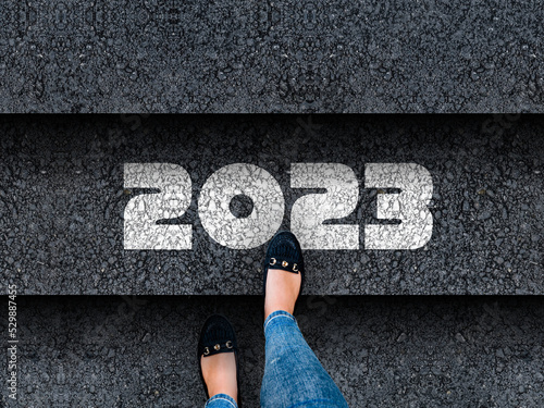 happy new year 2023. Woman legs in sneakers standing next to stairs with number 2023 