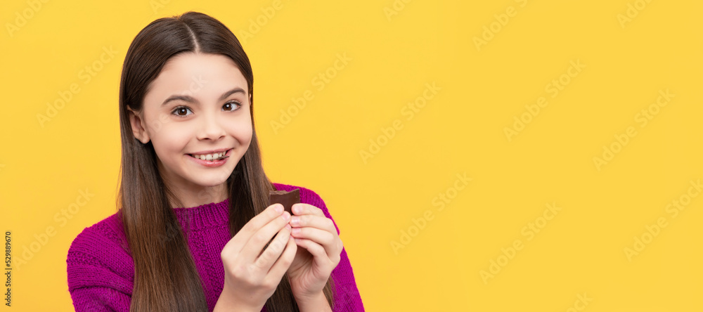 Happy girl child enjoy eating chocolate snack yellow background, tasty. Horizontal poster of isolated child face, banner header, copy space. Happy girl child enjoy eating chocolate snack yellow background, tasty. Horizontal poster of isolated child face, banner header, copy space.
