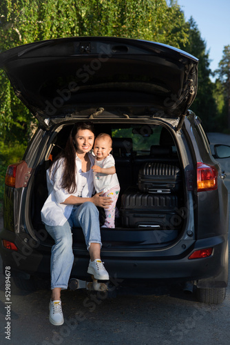 Car journey. Travel with a child by car. Mother and daughter sit in a car with an open trunk