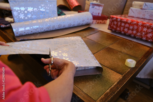 A Unrecognizable woman cutting out Christmas paper to wrap presents.