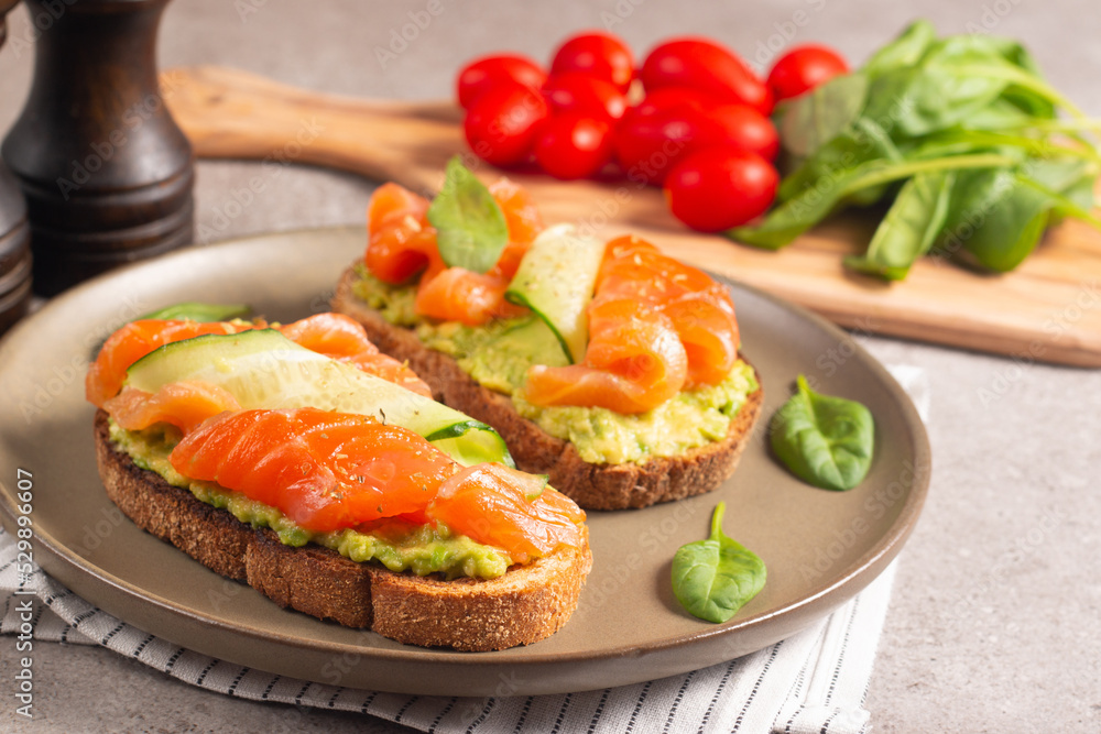 Two tasty open salmon sandwiches with avocado and cucumber. Morning healthy breakfast. Top view. Two tasty open salmon sandwiches with avocado and cucumber. Morning healthy breakfast. Top view.