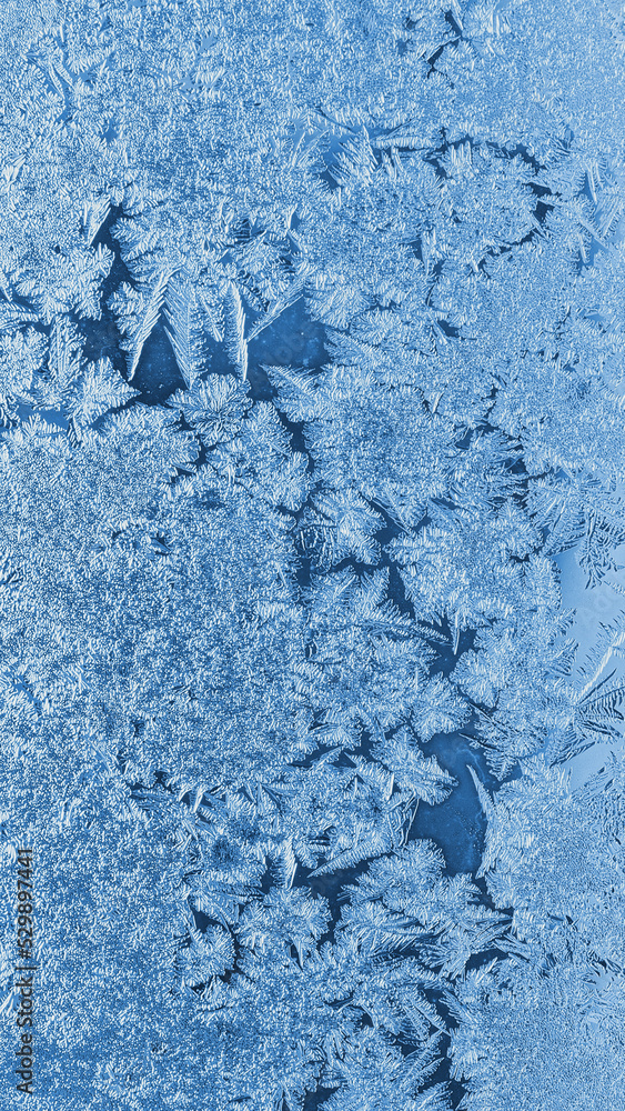 Abstract Christmas vertical background. Ice crystals on frozen window glass. Frost drawing. Winter pattern. Blue mobile phone tinted wallpaper. Cold and crystal. Macro