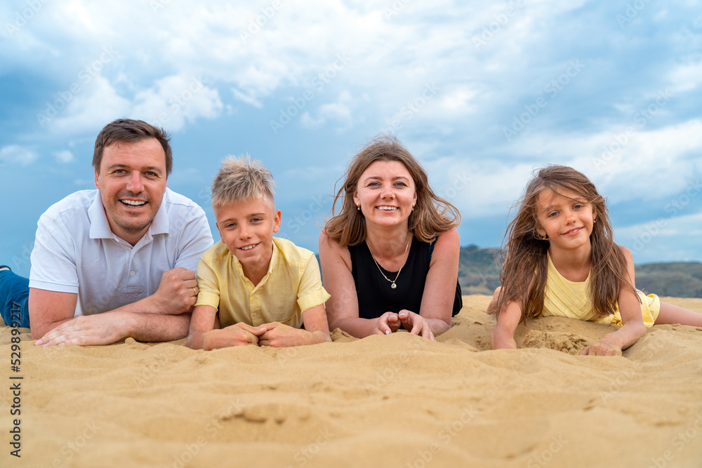 Happy family of mother, father, daughter and son having fun on sand dunes at beach on vacations together. Happy family of four lay on high dune at mountains. Fun happy lifestyle in summer leisure Happy family of mother, father, daughter and son having fun on sand dunes at beach on vacations together. Happy family of four lay on high dune at mountains. Fun happy lifestyle in summer leisure