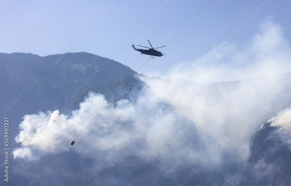 Fototapeta premium Wildfire Service Helicopter flying over BC Forest Fire and Smoke on the mountain near Hope during a hot sunny summer day. British Columbia, Canada. Natural Disaster