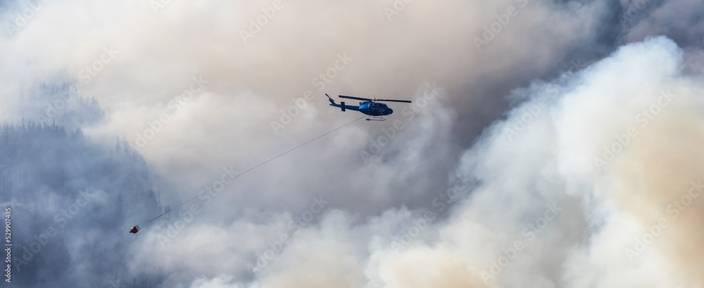 Wildfire Service Helicopter flying over BC Forest Fire and Smoke on the mountain near Hope during a hot sunny summer day. British Columbia, Canada. Natural Disaster Wildfire Service Helicopter flying over BC Forest Fire and Smoke on the mountain near Hope during a hot sunny summer day. British Columbia, Canada. Natural Disaster