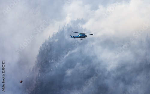 Wildfire Service Helicopter flying over BC Forest Fire and Smoke on the mountain near Hope during a hot sunny summer day. British Columbia  Canada. Natural Disaster