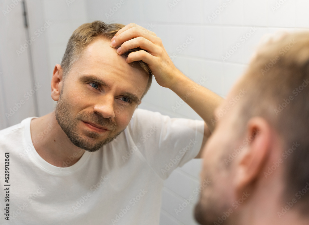 Middle aged caucasian white man with a short beard looks at his hair in the  mirror