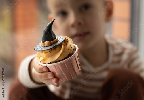 Boy with a cupcake in a shape of witch hat. Halloween and sweets concept photo