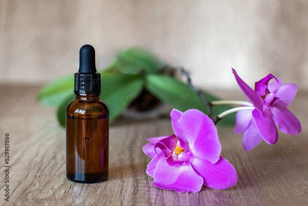 Glass brown bottle of serum with pipette on a wooden table with a blooming purple orchid, close up Glass brown bottle of serum with pipette on a wooden table with a blooming purple orchid, close up