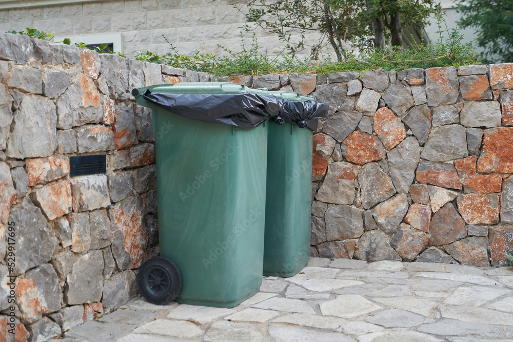 Obraz premium Green garbage cans next to the stone wall