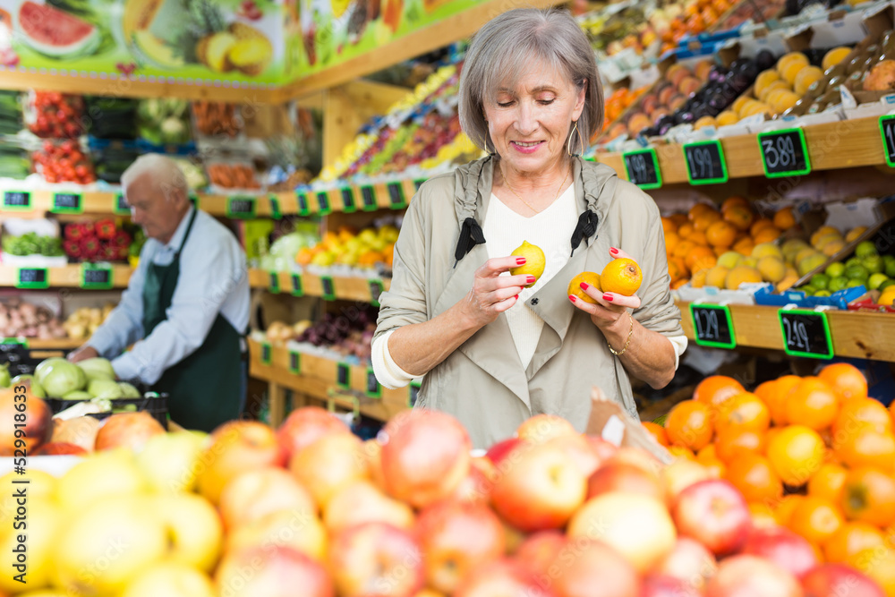 Portrait of adult woman choosing sweet apples and other fruit on counter of farmers market
