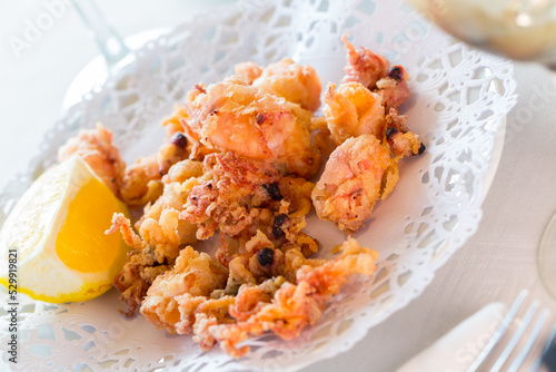Chipirones, battered fried baby squid served with lemon on white plate