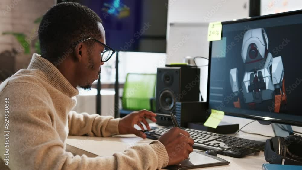 African American male artist designer draws on a tablet a 3D model of a dog robot for a computer game in the office of a project development studio. African American male artist designer draws on a tablet a 3D model of a dog robot for a computer game in the office of a project development studio.