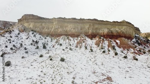 Forward tracking shot toward mesa style mountain in northern New Mexico on bright day with snow covered rocks and open desert