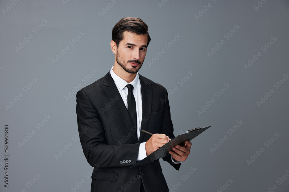Portrait of a business man in a stylish suit smile with teeth hands up handsome face on gray isolated background with tablet in hand. Business concept young businessman startup copy space. Portrait of a business man in a stylish suit smile with teeth hands up handsome face on gray isolated background with tablet in hand. Business concept young businessman startup copy space.