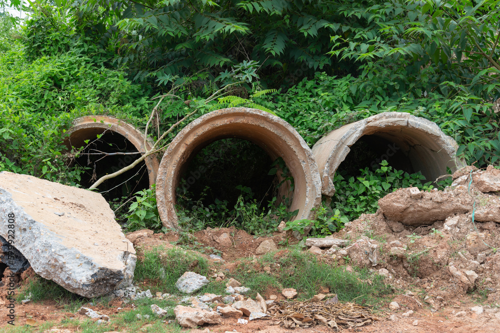 Old broken concrete cement pipe in grass, Old concrete pipes, Cracked and deteriorated sewer pipes are left or placed on the ground. Old broken concrete cement pipe in grass, Old concrete pipes, Cracked and deteriorated sewer pipes are left or placed on the ground.