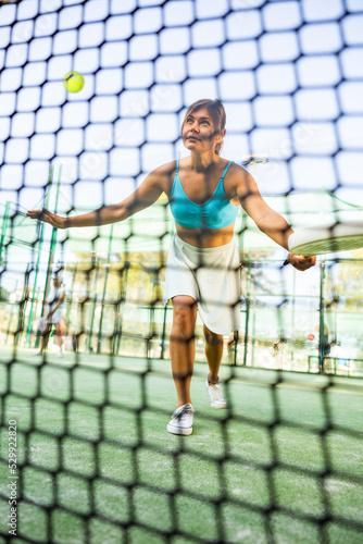 Caucasian woman in tank top and skirt playing padel tennis match during training on court.