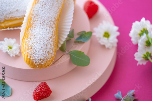  Eclairs cakes. Custard cakes with in powdered sugar on a pink podium on a Fuchsie background.Summer desserts. photo