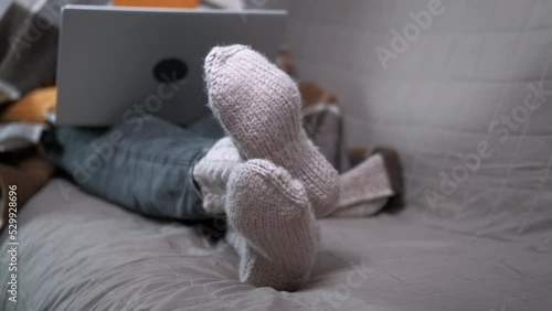 Relax in warm socks with computer. A calm child lay on the sofa in knitted clothes with her notebook. A concept of cozy time during winter period. photo