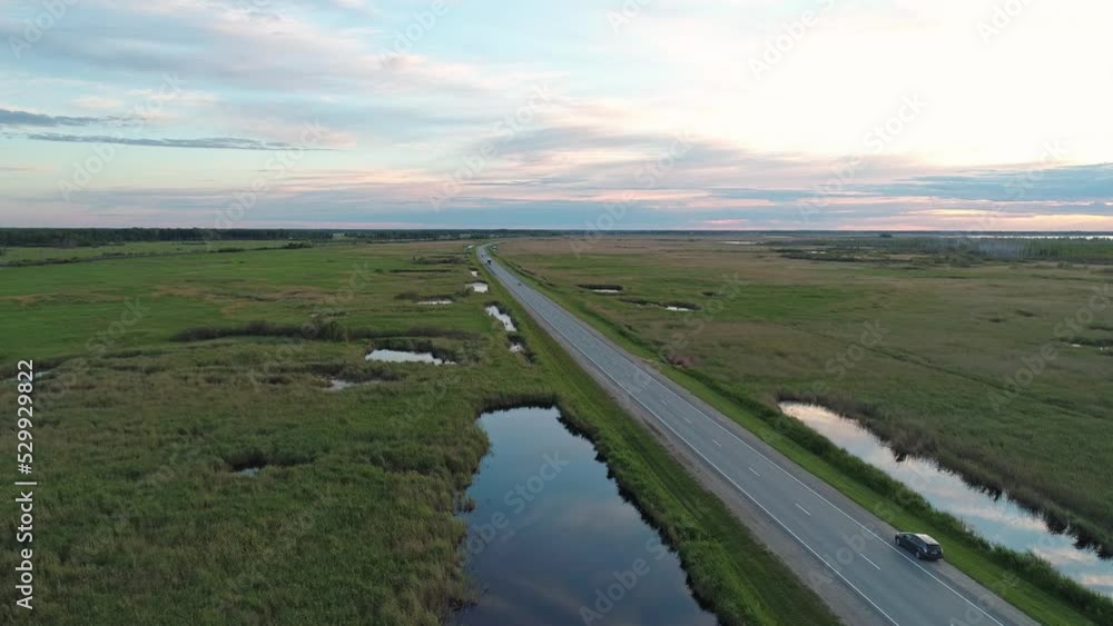 Aerial view of an intercity road with traffic between green fields in marshland. Beautiful summer landscape. Aerial view of an intercity road with traffic between green fields in marshland. Beautiful summer landscape.