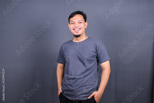 Handsome asian man wearing grey tshirt over grey background looking confident at the camera.