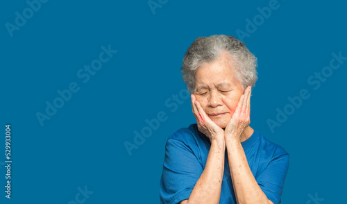 Senior woman suffering from a toothache while standing on a blue background