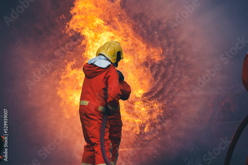 Firefighter Rescue training in fire fighting extinguisher. Firefighter fighting with flame using fire hose chemical water foam spray engine. Fireman wear hard hat, safety suit uniform for protection