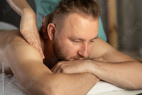 relaxed handsome man having body massage at spa salon. bearded young man attending modern male spa  laying on massage table  getting healing body procedure