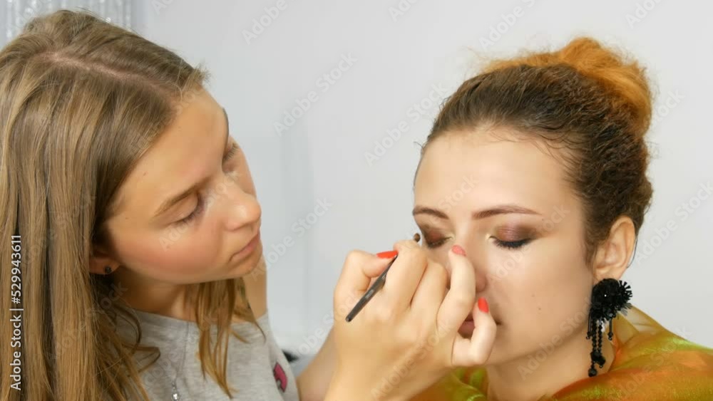 Young intern stylist make-up artist doing makeup on model in the studio Young intern stylist make-up artist doing makeup on model in the studio