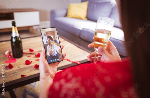 Biracial young couple with champagne dating online through smart phone on valentine day