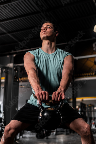 Caucasian man training in the gym performing training. Man lifting a kettlebell with a lot of effort. High quality photo