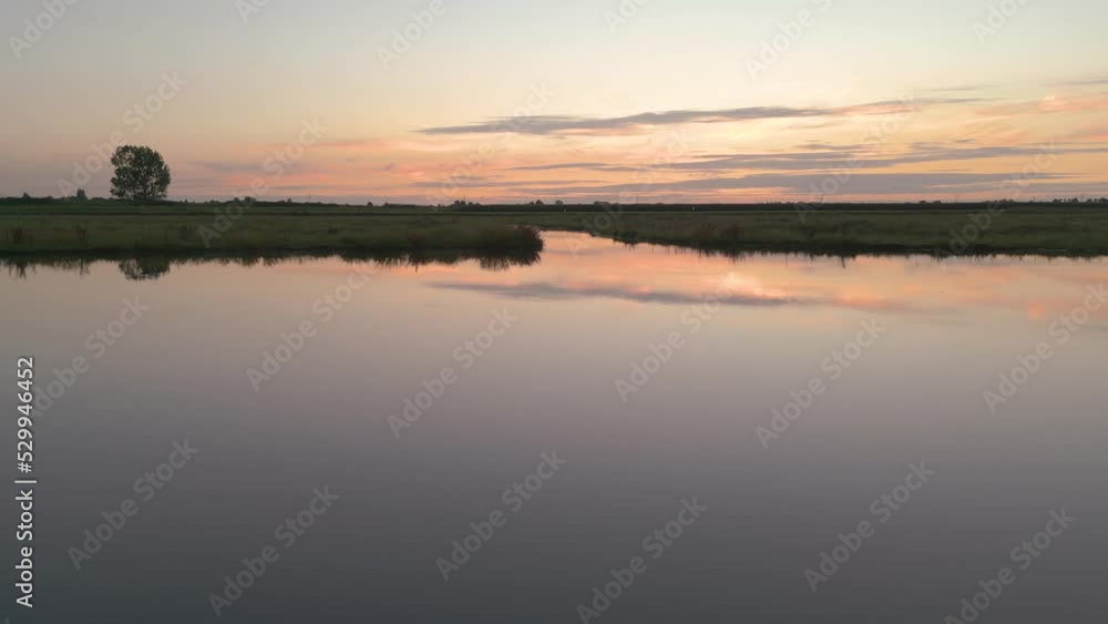 Dolly, Aerial shot over a green field with a lake at sunset. Dolly, Aerial shot over a green field with a lake at sunset.