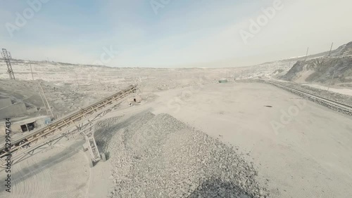 FPV drone view of  Conveyors in a quarry. There are heaps of rubble nearby. Next to the train, the wagons are filled with rubble.

