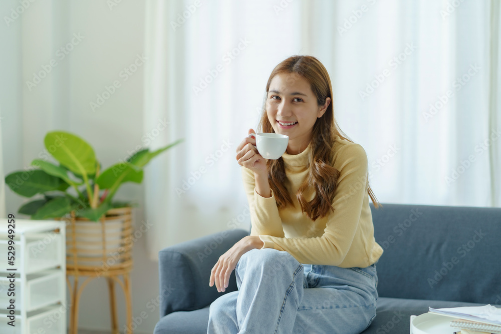 Beautiful young Asian woman is relaxing at home this morning happily with her favorite cup of coffee in a bright morning. Beautiful young Asian woman is relaxing at home this morning happily with her favorite cup of coffee in a bright morning.