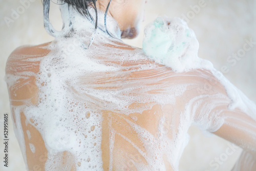 Woman showering. Headshot, Asian woman taking a shower. Cropped image of beautiful naked young woman rubbing body with foam and taking shower in bathroom.
