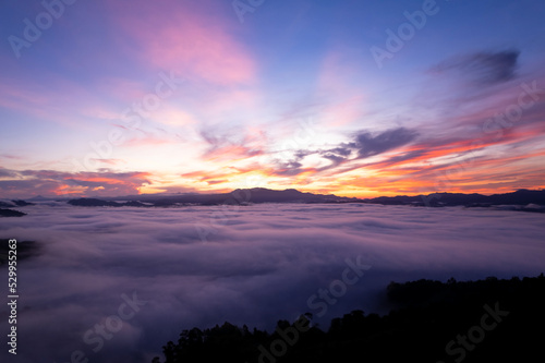 Aerial view of flowing fog waves on mountain tropical rainforest beautiful sunrise or sunset sky,Bird eye view image over the clouds Amazing nature background with clouds and mountains in Thailand